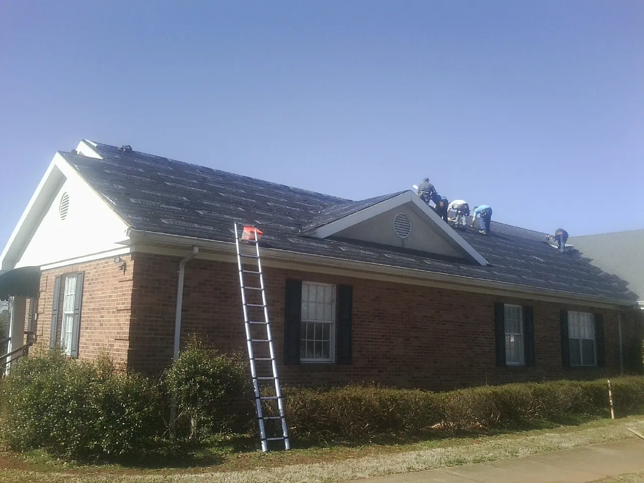 Crew tearing shingles off a brick ranch roof with a ladder set — Emergency Roof Repair work by our crew in Kearneysville
