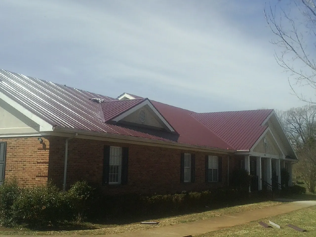 Red metal roof with gabled entries on a long brick building, from a Hail Damage Roof Repair job in Kearneysville