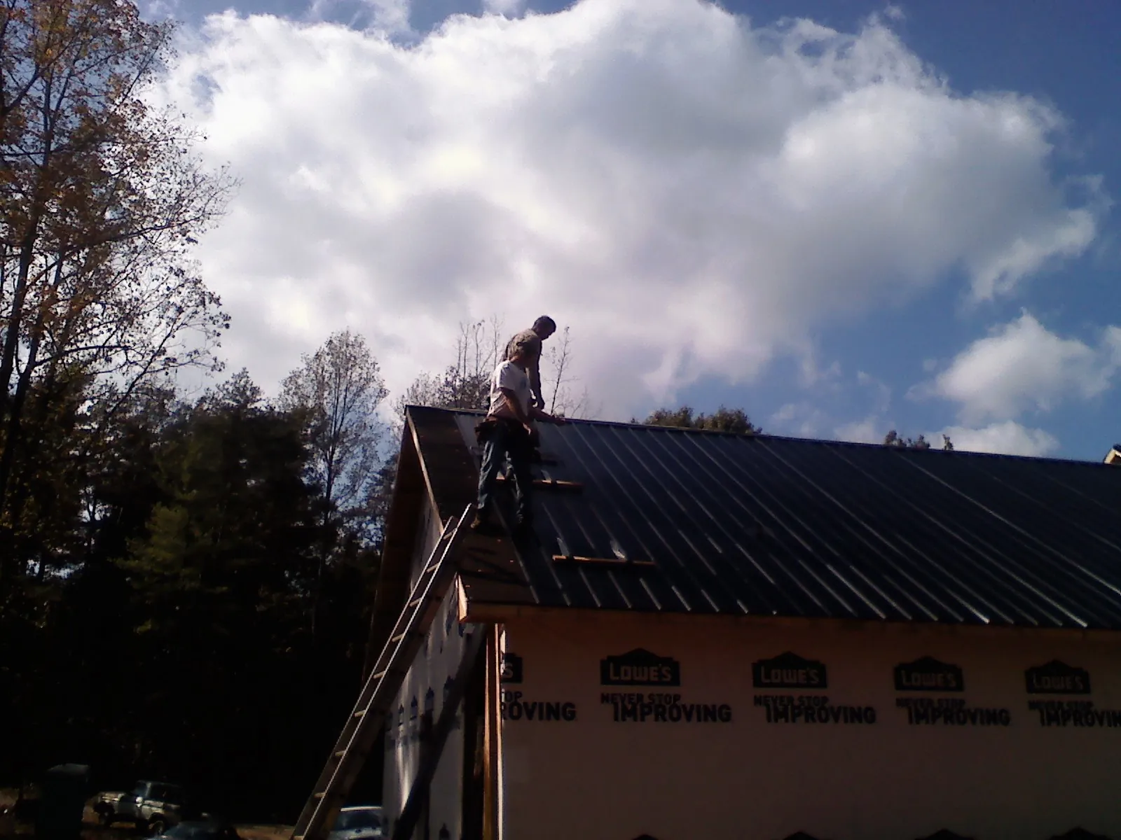 Roofer fastening dark metal panels high against a cloudy sky, from a Roof Inspection job in Kearneysville