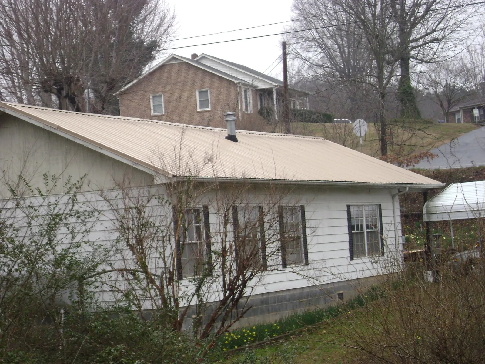 Tan metal roof on a white sided house set into a hillside — Commercial Roofing by Roofing Brothers in Kearneysville